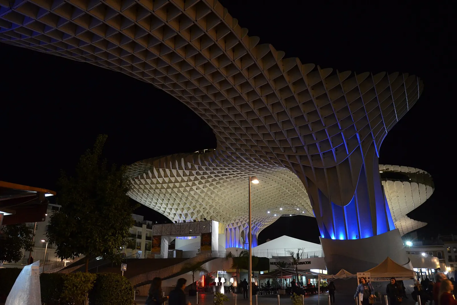 The lattice roof of the Metropol Parasol curving over the street-level arcade at night, with blue light on the columns