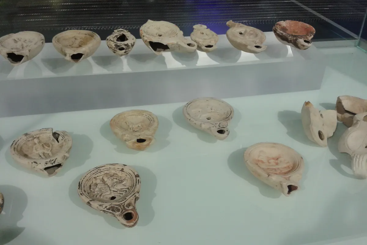 Roman oil lamps with moulded discs, arranged in rows inside a glass display case at the Antiquarium beneath the Metropol Parasol