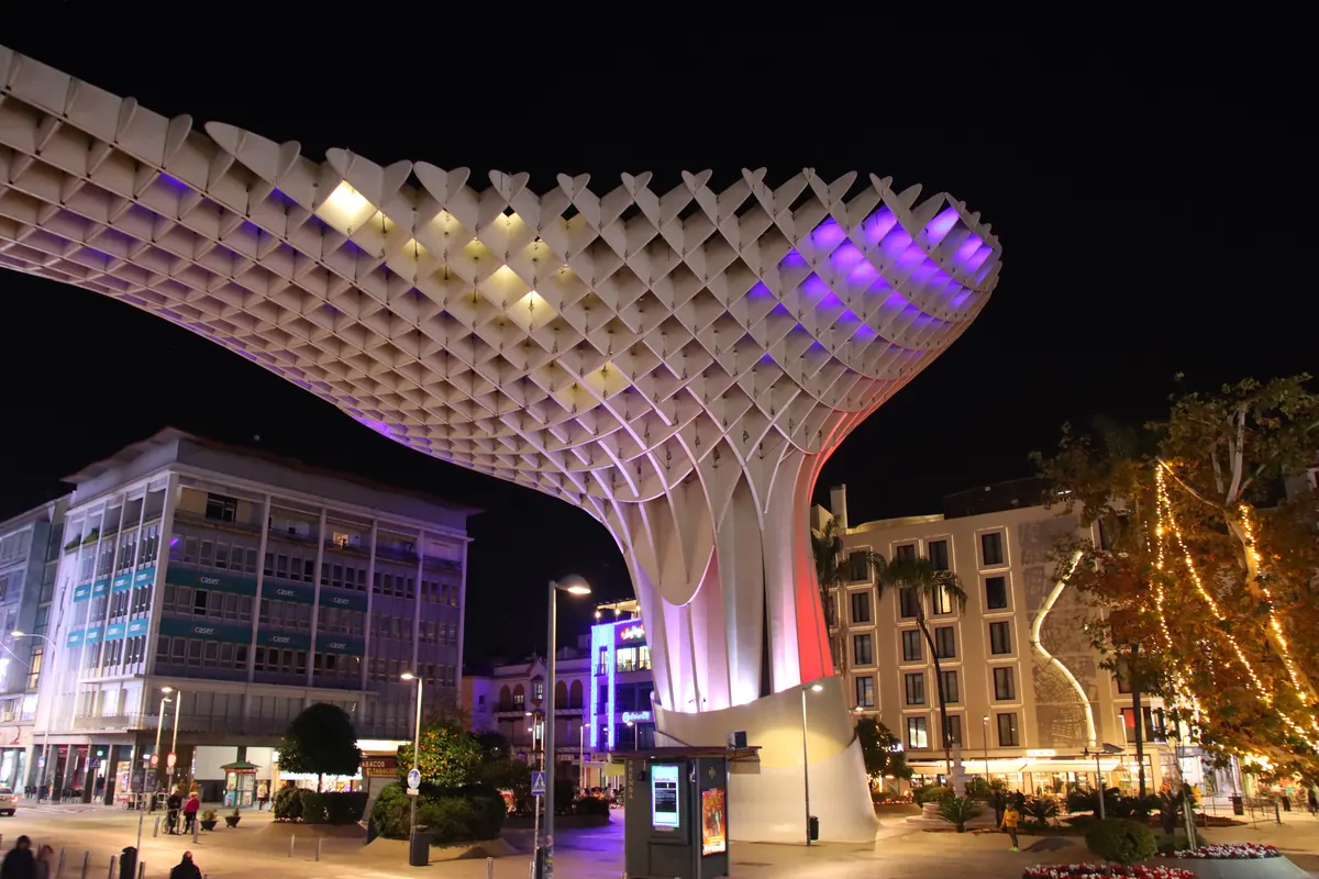 The Metropol Parasol in Seville at night, its pale timber lattice lit in violet and gold above Plaza de la Encarnación